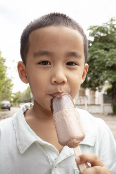 关闭脸亚洲男孩吃巧克力冰淇淋与幸福脸