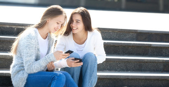 两个快乐女青少年会说话的在一起的街与车手机坐着的楼梯