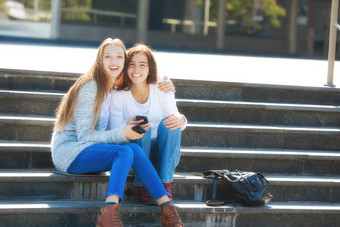 两个快乐女青少年会说话的在一起的街坐着的楼梯