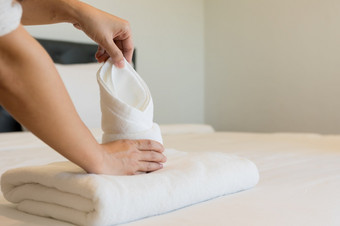 年轻的酒店女仆把软毛巾床上用品和毛巾酒店更清洁的是放置清洁白色毯子的床上与枕头的卧室的早....软毛巾卧室