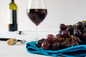 特写镜头群红色的葡萄和玻璃红色的酒与酒瓶蓝色的桌布特写镜头群红色的葡萄和玻璃红色的酒与酒瓶