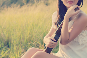 美丽的女人坐着手拥抱小提琴的草地