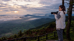 女人旅游持有数码单反相机相机看的美丽的自然景观太阳雾山的冬天在日出高的观点府ruea国家公园游荡省泰国女人是看的美丽的自然