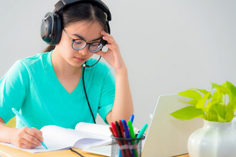 亚洲女人学生<strong>十</strong>几岁的女孩与眼镜耳机坐着看严重的阅读书担心使用移动PC电脑表格<strong>学习</strong>在线研究教育从类大学首页亚洲女人严重的阅读书<strong>学习</strong>在线