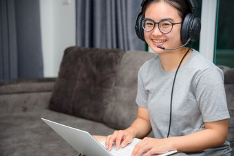 亚洲年轻的女人学生与耳机坐着的沙发微笑看快乐研究在线类大学<strong>学习</strong>互联网教育<strong>十</strong>几岁的女孩工作距离移动PC电脑从首页距离<strong>学习</strong>在线从首页