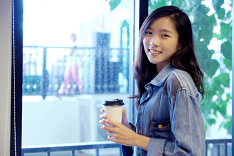 亚洲女人与取走了咖啡杯快乐亚洲女孩看相机和持有咖啡而站窗口亚洲女大学学生和disposeble杯咖啡商店咖啡馆背景人食物和喝lifestlye