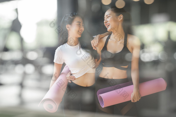 十几岁的女孩朋友走持有紫色的瑜伽垫后给瑜伽的健身房模糊的前景照片通过玻璃窗口年轻的亚洲女人会说话的和笑健身设施