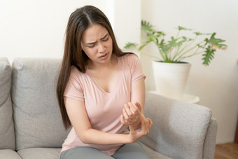 亚洲女孩有手腕疼痛坐着沙发首页年轻的女孩有疼痛关节炎健康和疾病概念