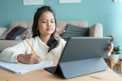教育亚洲女孩学习与在线导师通过的互联网平板电脑数字首页早....亚洲孩子们看电脑和写家庭作业概念在线学习首页