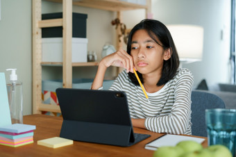 无聊的亚洲女孩研究在线通过的互联网平板电脑而坐着表格首页晚上亚洲小学学校孩子们看电脑平板电脑概念距离学习首页