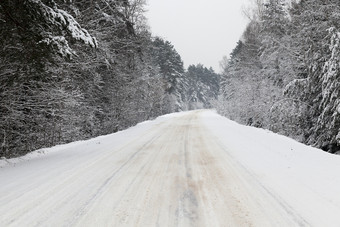 沥青路拍摄的冬天季节在大降雪的路转正确的通过的森林冬天路下的雪