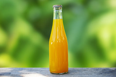 橙色汁包装玻璃瓶表格前使木和绿色自然背景