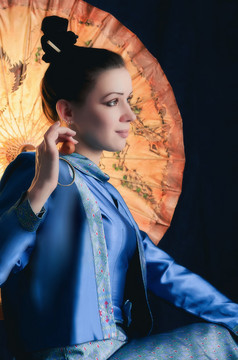 程式化的肖像年轻的微笑女人坐着与的中国人黄色的纸伞对黑暗背景年轻的女人坐着与中国人伞