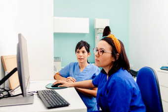 两个护士使用电脑x射线房间一个他们穿眼镜和坐着附近的桌子上两个护士使用电脑x射线房间
