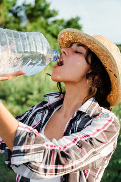 农民女人喝水从塑料瓶作物场