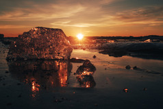 块美丽的透明的冰粉红色的和琥珀色的颜色珠宝闪亮的冻海滨的日落