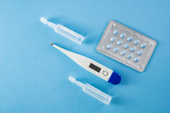 泡包蓝色的药片灯泡和温度计蓝色的背景:医疗保健和医疗概念