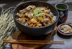 日本猪肉大米碗与蛋和洋葱donburi服务与腌姜和绿色茶木表格日本食物风格