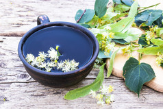 杯林登茶附近的石灰花的背景老董事会林登花和杯茶Herbal茶冷和流感补救措施杯林登茶附近的石灰花的背景老董事会林登花和杯茶