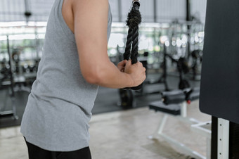 锻炼概念的高额男人。与他的灰色体育运动前和黑色的裤子站仍然抓住的绳子和拉向下