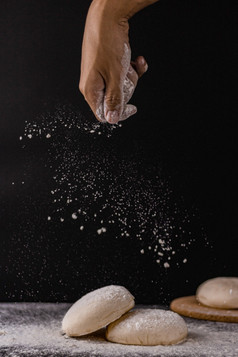 面包概念几好面团和面粉被的中间的黑色的背景与手洒面粉灰尘的面包