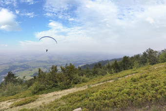 男人。飞行滑翔伞在的坡的喀尔巴阡山脉的山对蓝色的天空的阴霾的天空飞行滑翔伞对的蓝色的天空的早....雾的喀尔巴阡山脉的山