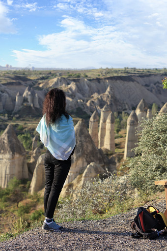 年轻的女孩绿<strong>松石</strong>围巾她的肩膀站的边缘悬崖和看起来的山峡谷和蓝色的天空卡帕多西亚年轻的女孩站的边缘悬崖和看起来的地平线的山山谷卡帕多西亚和的蓝色的天空