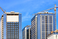 的建设现代住宅混凝土建筑与玻璃外观塔起重机使用的蓝色的天空反映了的窗户的建筑水平图像与复制空间的玻璃外观反射的蓝色的天空和起重机附近现代混凝土建筑下建设