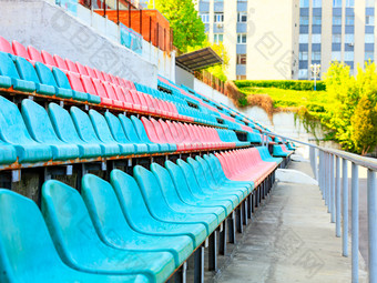 的有<strong>节奏</strong>的行空绿松石和红色的塑料椅子老体育体育场对的背景阳光的背景的有<strong>节奏</strong>的行座位的老体育体育场