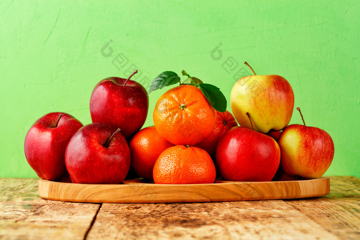 红色的成熟的苹果和官员与绿色叶子谎言木托盘老木表格光绿色背景图像与复制空间红色的成熟的苹果和橘子与绿色叶子谎言木托盘老木表格与光绿色背景
