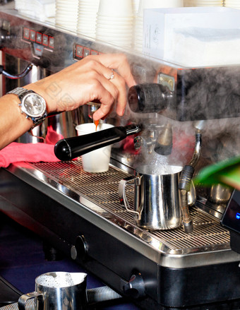 手夫人咖啡师对于沸腾水成金属杯子从咖啡机使拿铁咖啡表示机户外咖啡馆的咖啡师手对于沸腾水成金属杯子为使拿铁咖啡使喝