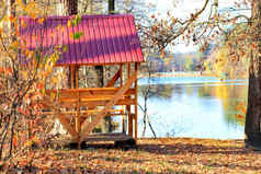 简单的木露台与表格和野餐长椅与红色的屋顶使金属站在户外对背景下降叶子附近森林湖温暖的秋天一天复制空间木阿伯与表格和野餐长椅的开放空气的背景下降叶子附近森林湖