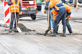 路工人橙色工作服铲碎片从的老人行道上的巷道与铲子路工人是铲的老路表面的巷道