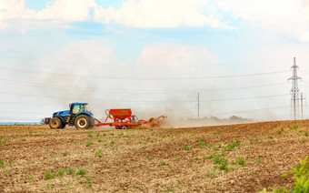 农业拖拉机与现代播种机新鲜耕种场春天一天蓝色的拖拉机和红色的播种机的场复制空间农业拖拉机与落后播种机培养的土壤的场应用的必要的化肥