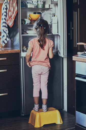 小女孩站蔡尔兹凳子前面打开冰箱看为冰面霜在食物产品真正的人真实的的情况下