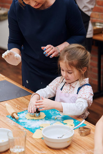 小女孩与她的妈妈帮助切割的面团心形状为的饼干孩子们采取部分烘焙车间烘焙类为孩子们有抱负的小厨师女孩学习烹饪结合和激动人心的准备成分真正的人真实的的情况下