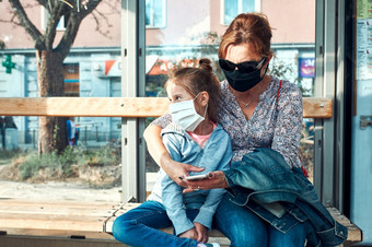 女人和她的孩子等待为公共<strong>汽车</strong>坐着公共<strong>汽车</strong>停止公共运输妈妈。和她的小女儿穿脸面具<strong>封面</strong>口和鼻子在流感大流行冠状病毒爆发