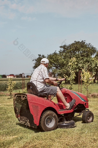男人。割草他的草坪上使用骑剪草机男人。维护草他的花园旁边房子男人。割草他的草坪上使用骑剪草机