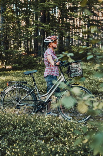 活跃的女人支出免费的假期时间自行车旅行森林阳光明媚的夏天一天女人穿自行车头盔和手套持有自行车与篮子站后面的模糊树叶子活跃的女人支出免费的夏天假期时间自行车旅行森林