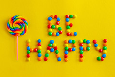 文本快乐从色彩斑斓的糖果和彩色的棒棒糖黄色的背景