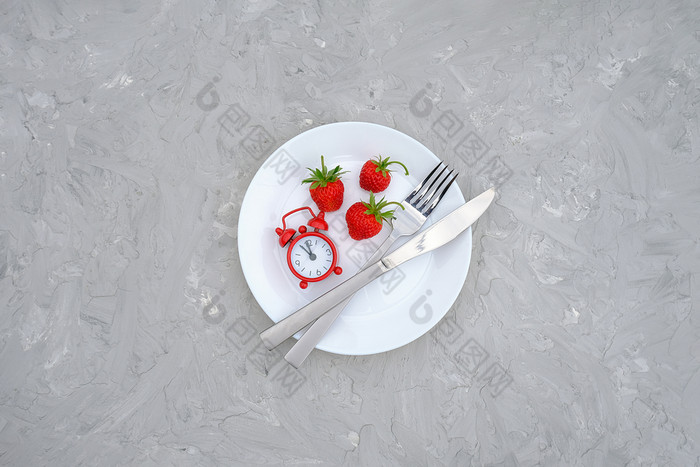 红色的成熟的草莓浆果白色板餐具和红色的报警时钟灰色的石头背景表格前视图平躺复制空间模板概念饮食和排毒时间夏天菜单时间红色的成熟的草莓浆果白色板餐具和红色的报警时钟灰色的石头背景表格前视图平躺复制空间模