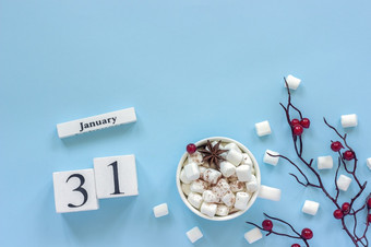 冬天作文白色木日历多维数据集数据1月杯可可棉花糖和装饰分支与红色的浆果蓝色的背景前视图平躺复制空间日历1月杯可可棉花糖和分支浆果