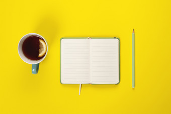 薄荷茶杯和花俏的笔记本与空空白页面明亮的黄色的桌子上从以上规划和设计概念前视图平躺复制空间模拟薄荷茶杯和花俏的笔记本与空空白页面明亮的黄色的桌子上从以上规划和设计概念