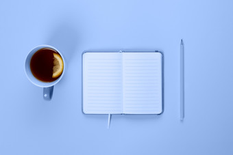 茶杯和花俏的笔记本与空空白页面蓝色的桌子上从以上规划和设计概念前视图平躺复制空间模拟茶杯和花俏的笔记本与空空白页面蓝色的桌子上从以上规划和设计概念