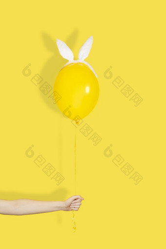 有创意的复活节最小的概念手持有黄色的气球兔子耳朵单色有创意的复活节最小的概念手持有黄色的气球兔子耳朵单色