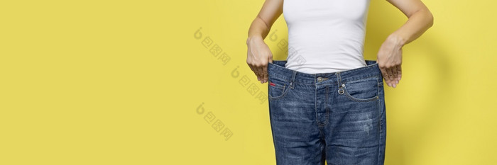的概念饮食适当的营养重量损失苗条的女人显示宽松的牛仔裤和她的损失重量女人白色t恤和超大的牛仔裤孤立的黄色的背景横幅与复制空间的概念饮食适当的营养重量损失苗条的女人显示宽松的牛仔裤和她的损失重量女人白色