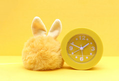 黄色的玩具皮毛兔子和黄色的塑料时钟黄色的纸背景复制空间
