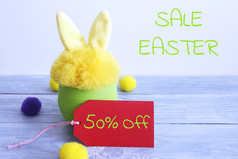 黄色的皮毛玩具兔子绿色塑料能灰色的木董事会和灰色的背景与的单词复活节出售红色的纸标签与的单词从和黄色的和紫色的羊毛球