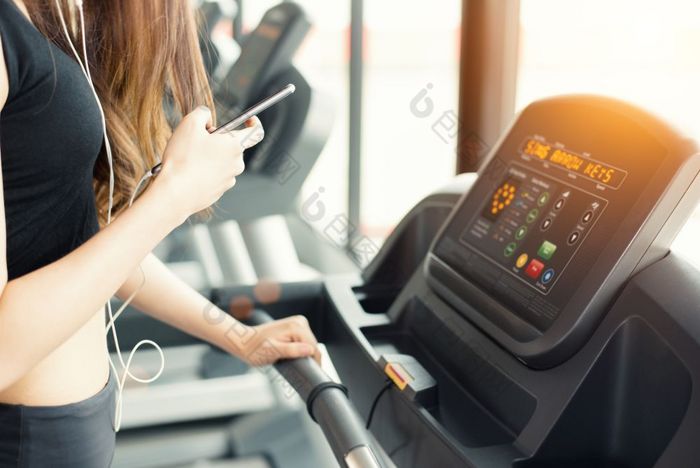 亚洲女人使用聪明的电话当锻炼强度培训健身健身房跑步机放松和技术概念体育锻炼和健康哪主题快乐和舒适的情绪