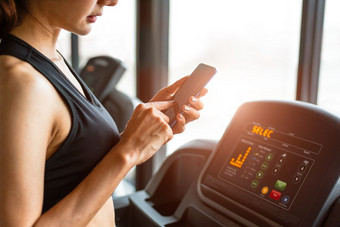 女人使用聪明的电话当锻炼强度培训健身健身房跑步机放松和技术概念体育锻炼和健康哪主题快乐人和舒适的应用程序